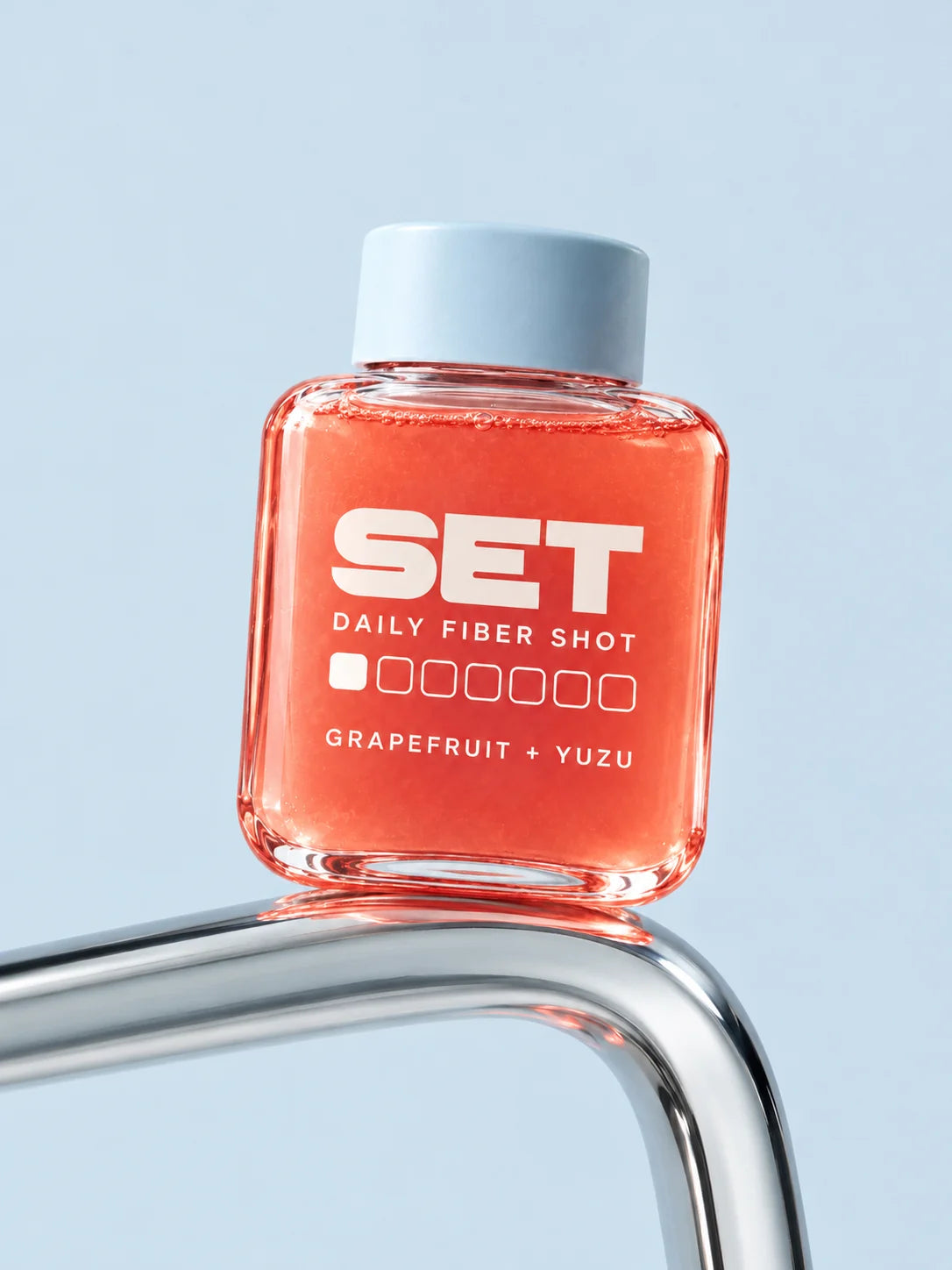 A SET grapefruit-yuzu shot with a pale-blue cap and coral juice balanced on curved chrome