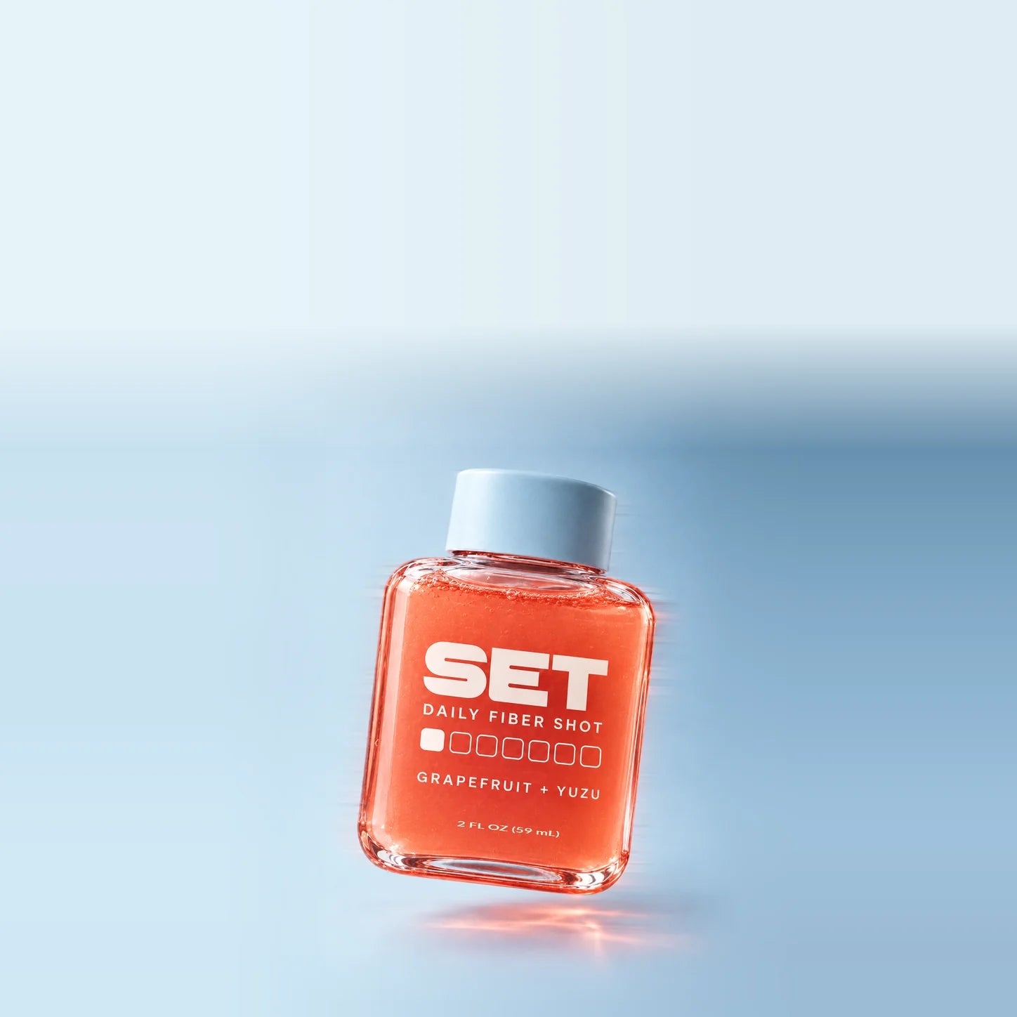 Close-up of a SET shot in motion, showing coral juice, clear bottle edges and a pale blue cap